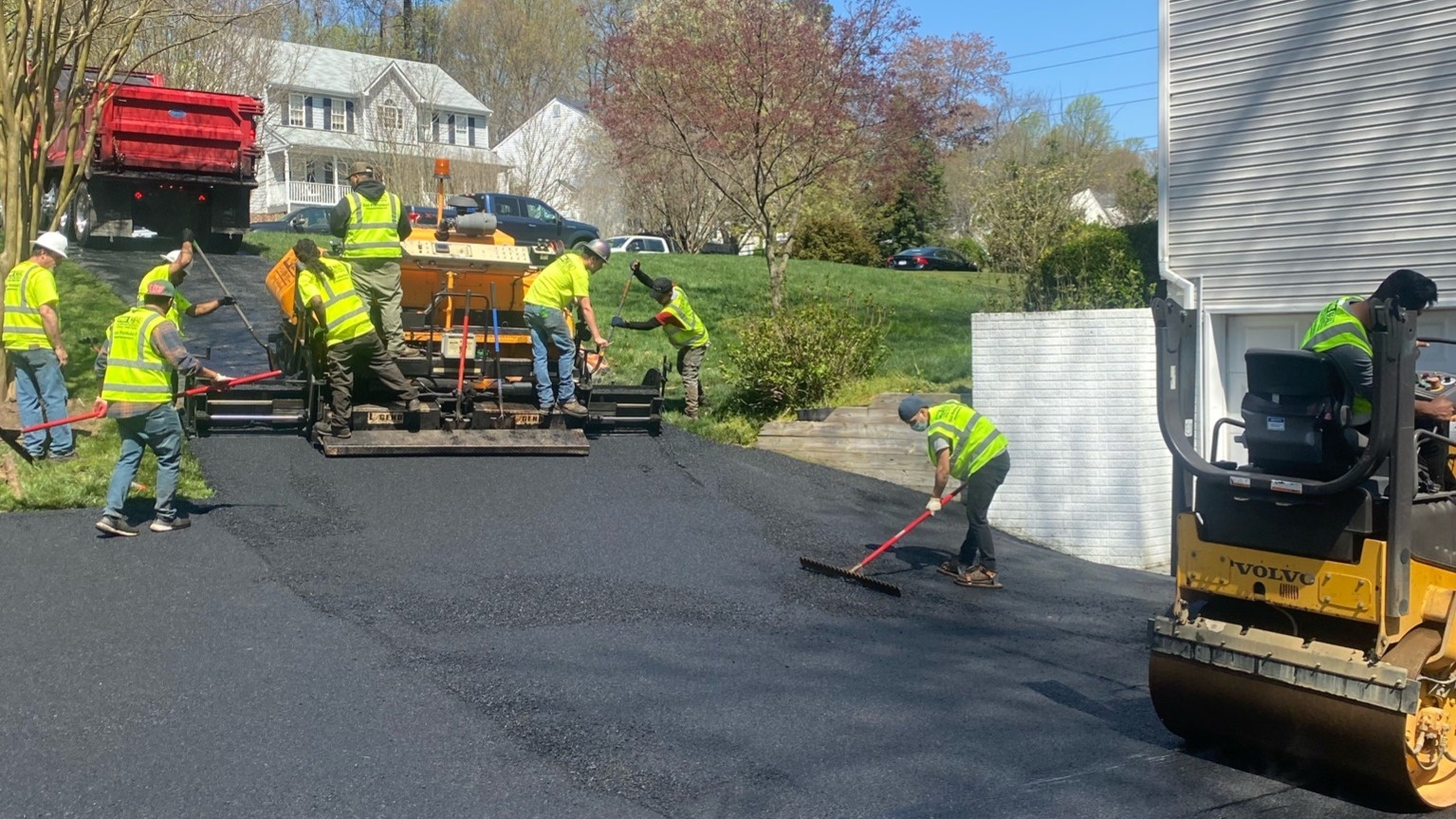 Asphalt paving crew installing a new residential driveway in Richmond, Virginia using a paving machine and roller.