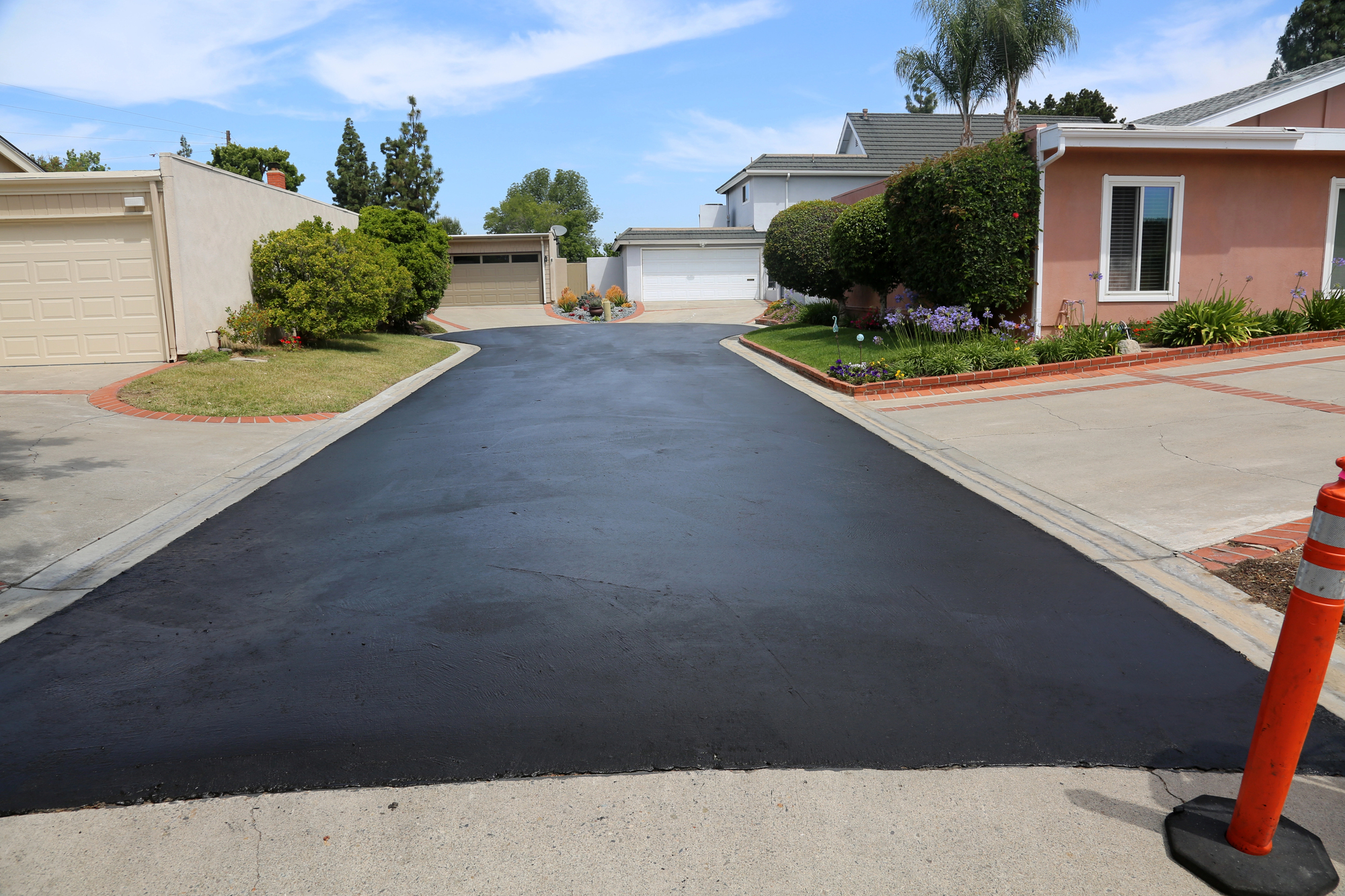 Freshly paved asphalt driveway in a residential neighborhood with garages and landscaped yards.